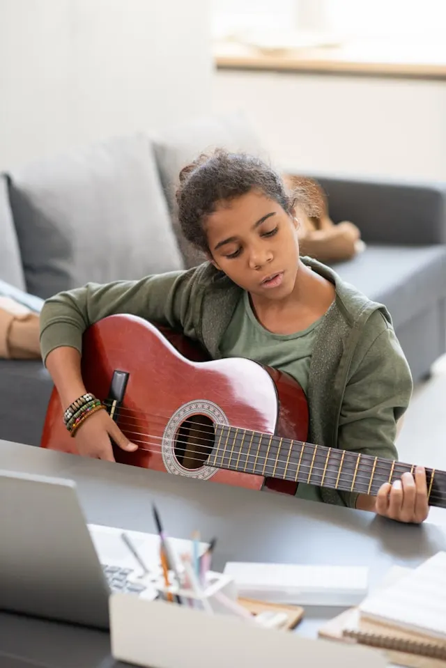 Child learning guitar at home with a laptop